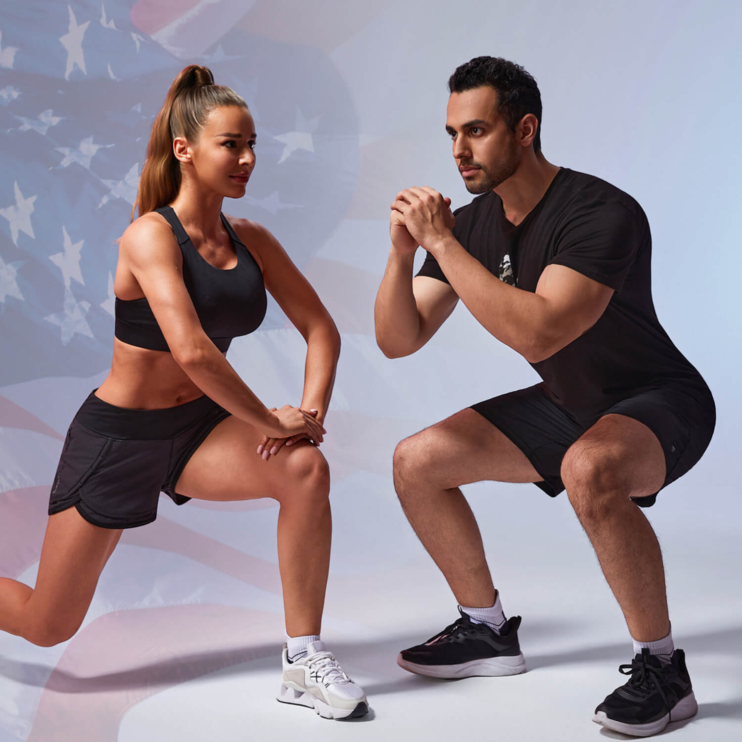 A woman and a man in athletic wear performing lunges and squats, showcasing black HYLETE shorts and workout gear against US flag background.