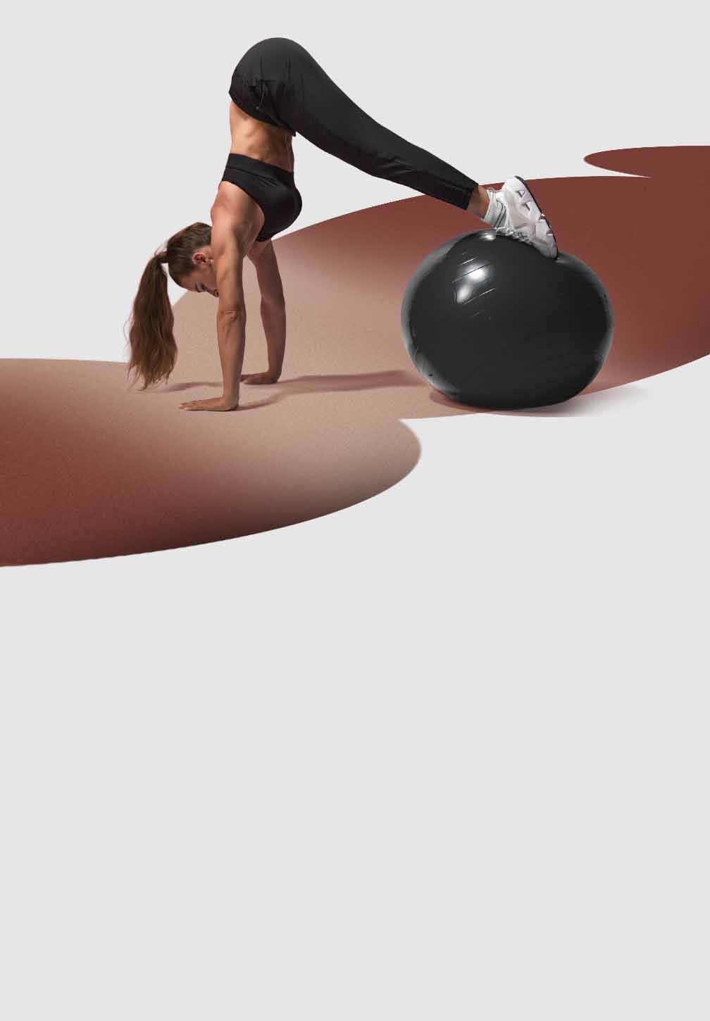 A woman in black Hylete Chase pant and a black sports bra is positioned on her hands and toes in a pike push-up or downward-facing dog variation. Her hands are on the floor, and her feet are balanced on a large, glossy black stability ball, creating an inverted V-shape with her body.