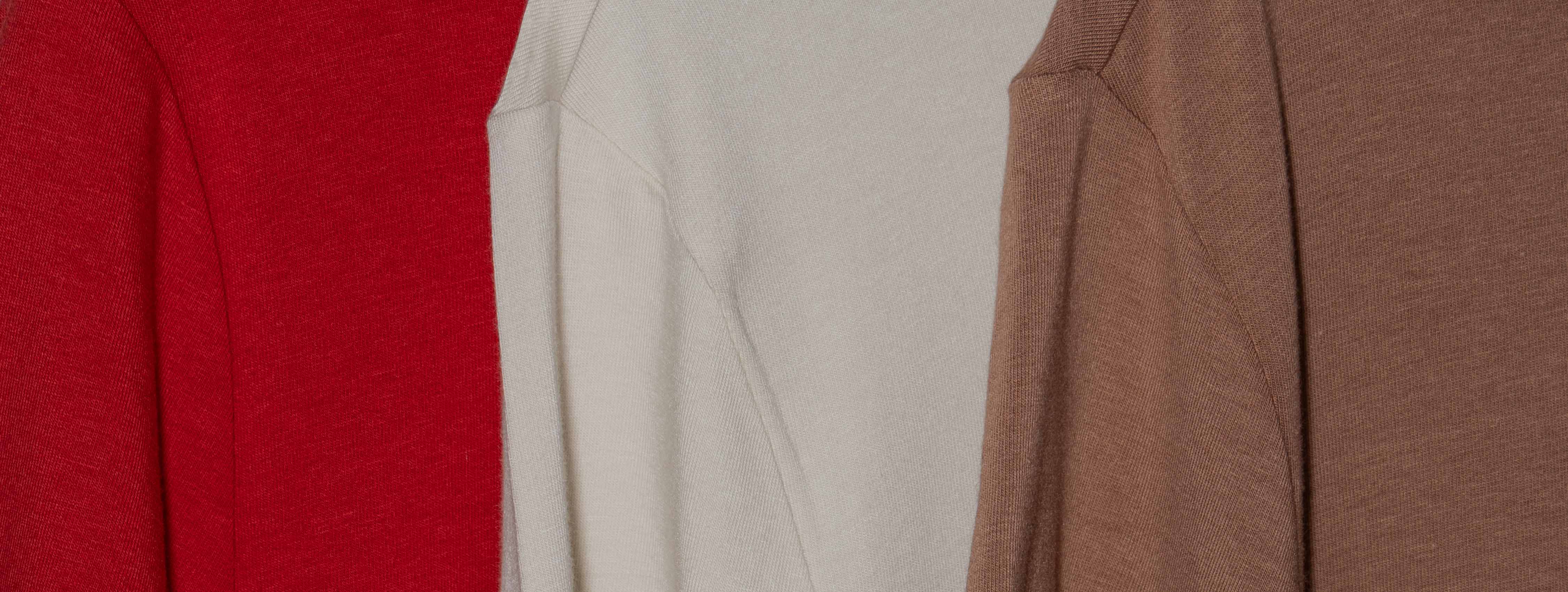Close-up shot shows three Hylete HY-Blend crew tees hanging side by side. From left to right, the colors are a crimson red, a bone white, and a raw umber.