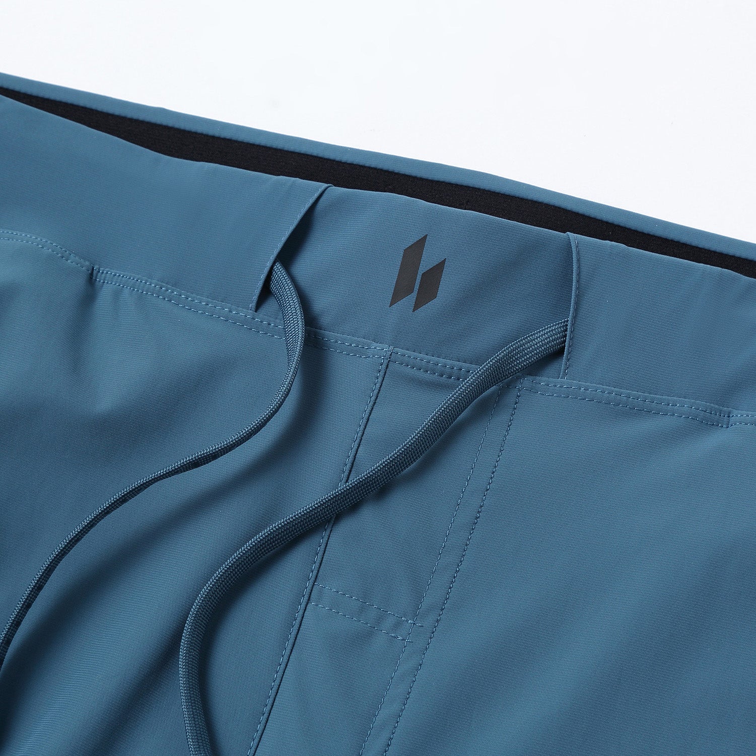 Close-up of HYLETE Ion II slate pants with a brand logo on a white background