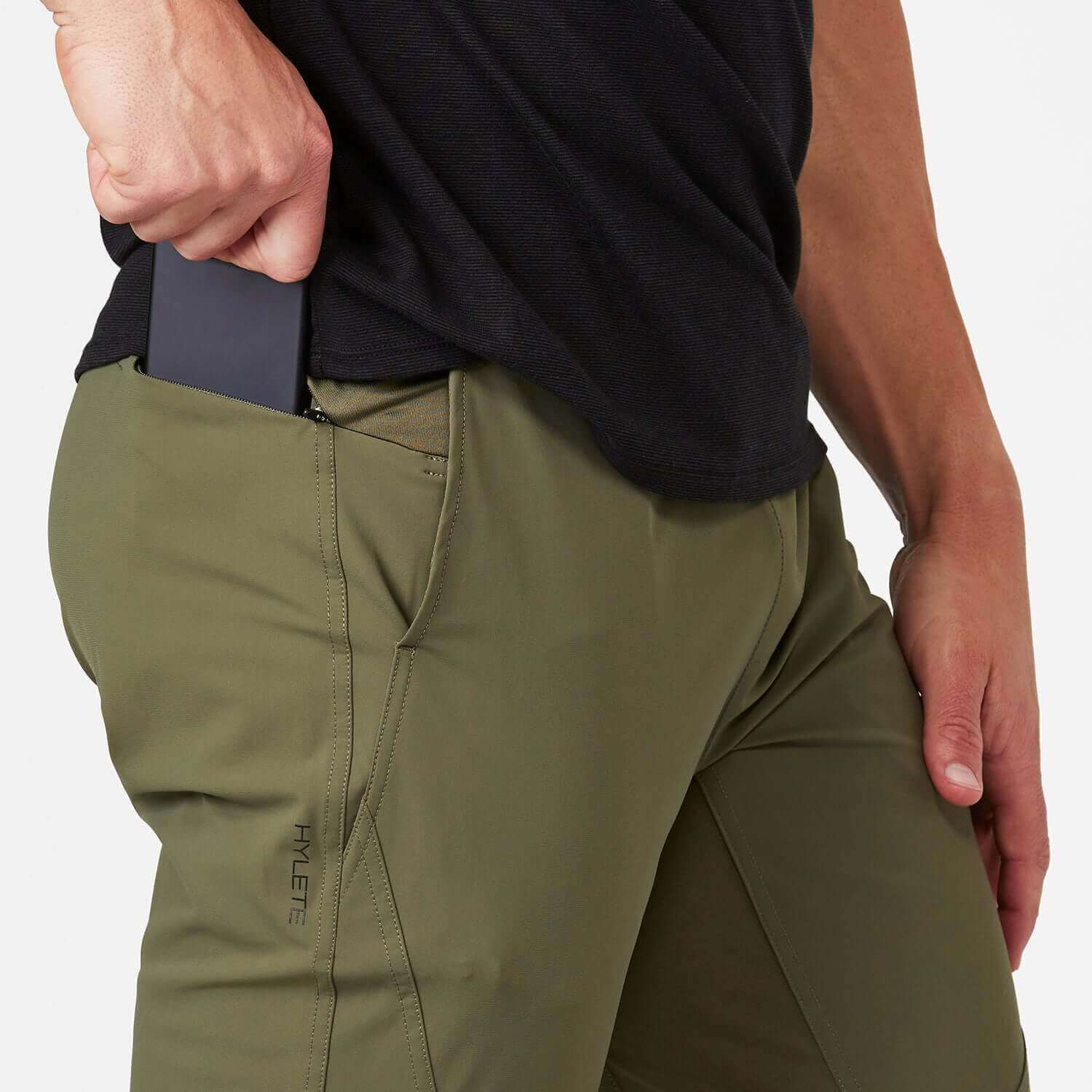 Man wearing Ion Pant Olive, retrieving a phone from the pocket, showcasing comfort and functionality for everyday wear.