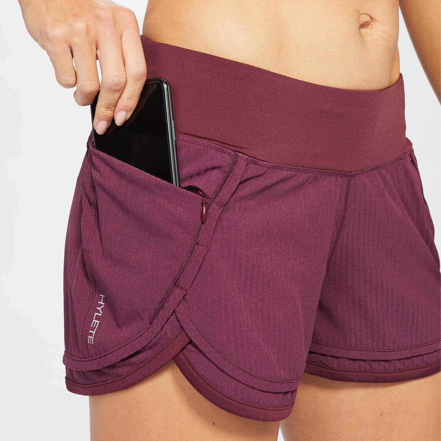 Woman wearing Iris Lined Short Raisin with a smartphone in the side pocket, showcasing comfort and utility for workouts.