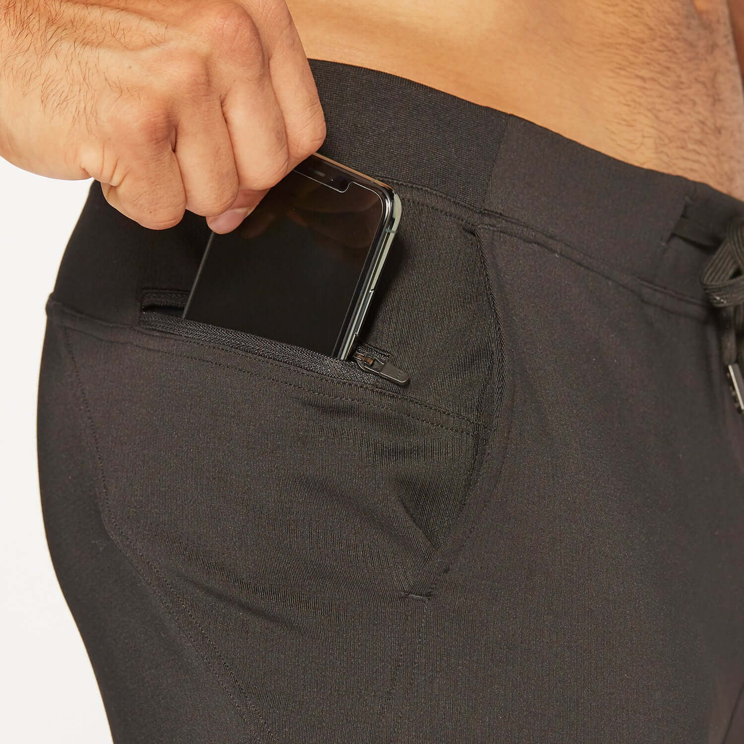 Person placing a smartphone into the pocket of Flexion II Jogger in black, showcasing functionality and style.