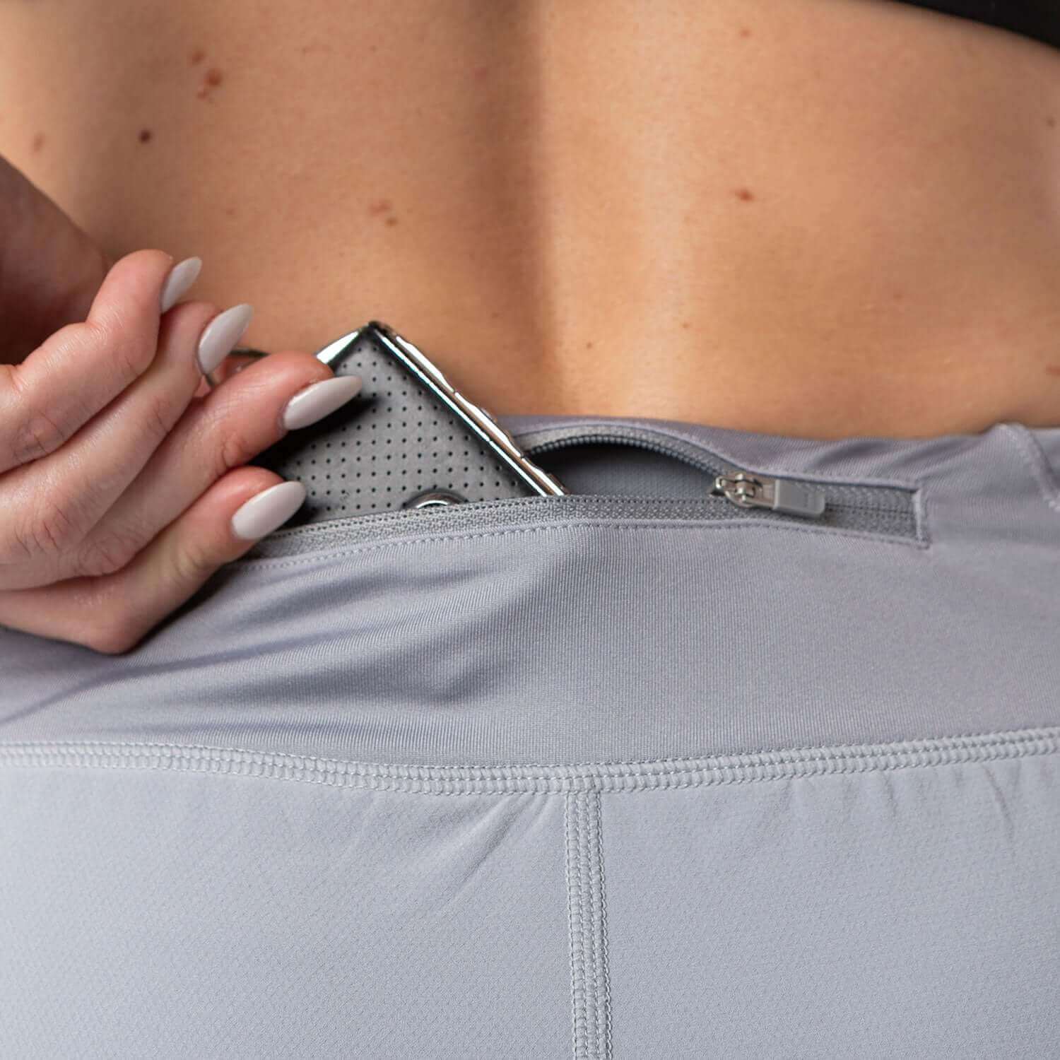Woman using zippered pocket in gray Vita Short for secure storage during workouts