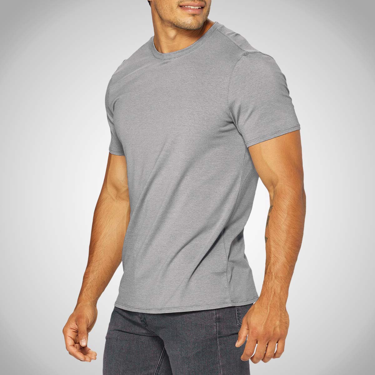 A man, shown from the chest down and facing to the right, wearing a gray HYLETE Icon II Crew Tee and dark gray jeans.