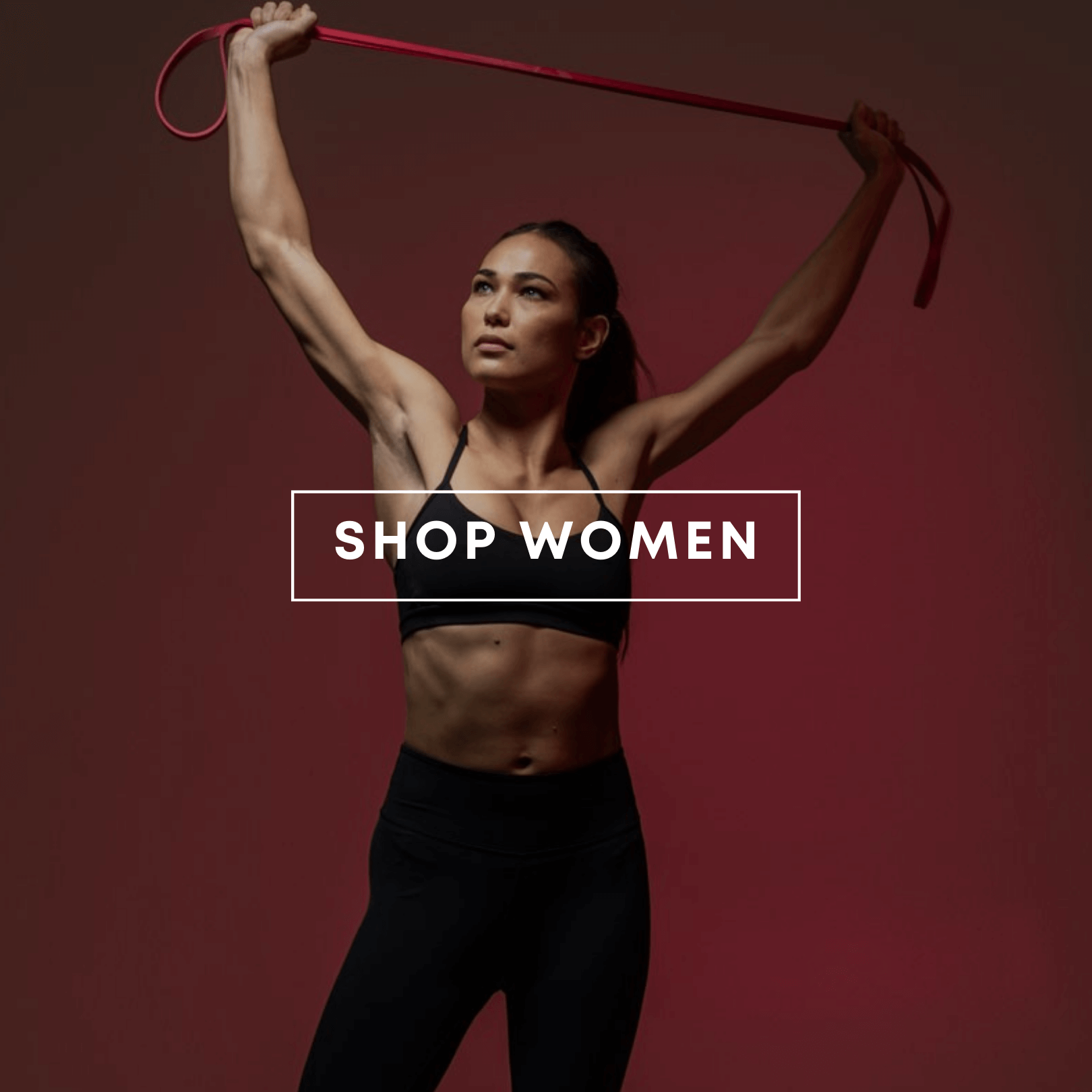 A fit woman in black HYLETE tights and sports bra poses holding a red fitness band overhead on a dark red background. Text overlay reads: "SHOP WOMEN".